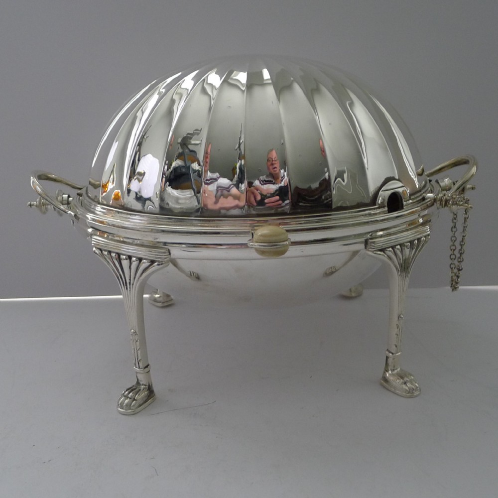 A Victorian silver-plated revolving breakfast dish featuring a fluted domed cover, twin side handles, and four cast claw legs.