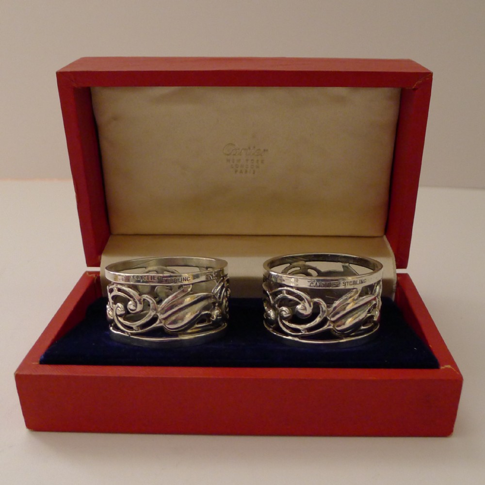 A pair of pierced sterling silver napkin rings with foliage motifs resting inside a red Cartier presentation box.