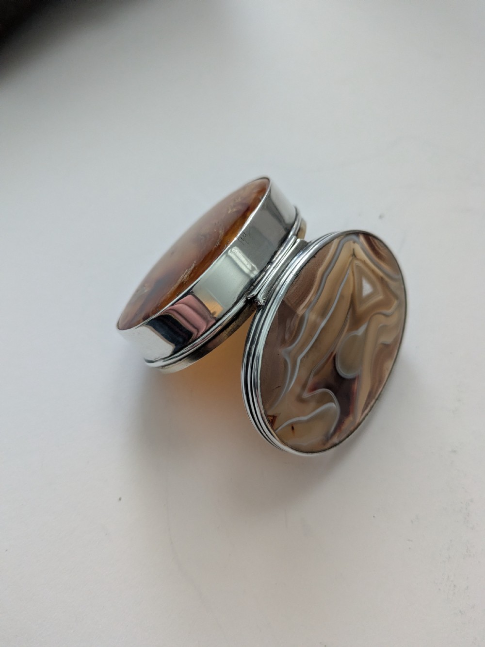An oval Edwardian sterling silver box featuring polished natural agate stone panels on the hinged top and base. View X