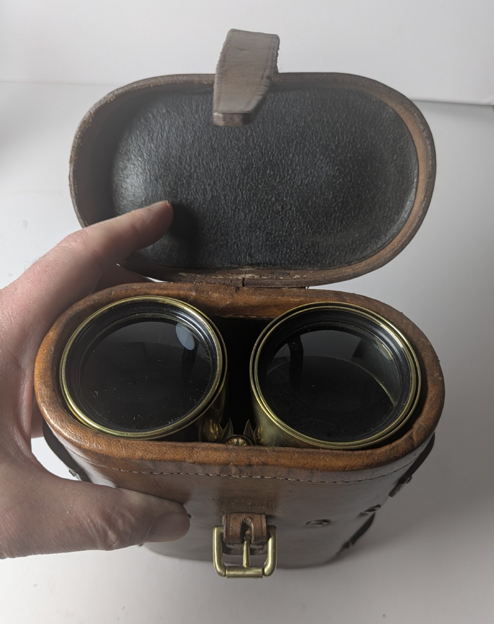 A pair of antique brass field binoculars with textured brown leather grips alongside a fitted brown leather carrying case with straps. View IV