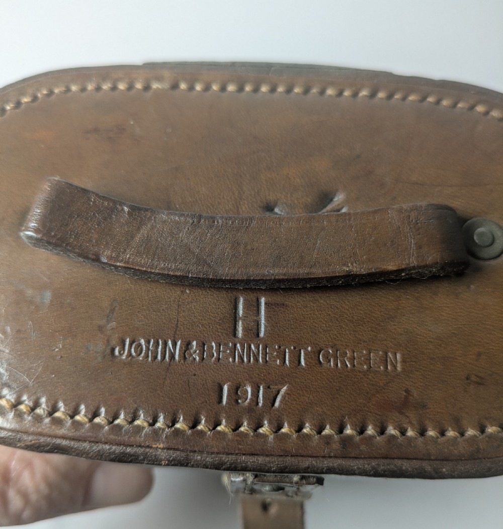 A pair of antique brass field binoculars with textured brown leather grips alongside a fitted brown leather carrying case with straps. View VI