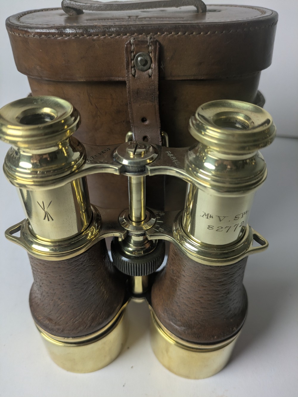 A pair of antique brass field binoculars with textured brown leather grips alongside a fitted brown leather carrying case with straps. View IX