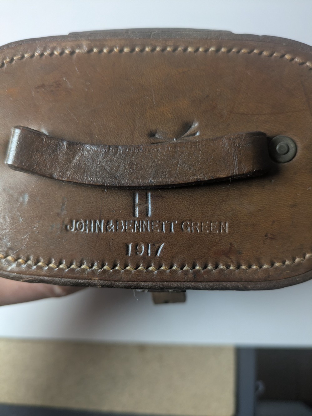 A pair of antique brass field binoculars with textured brown leather grips alongside a fitted brown leather carrying case with straps. View XIII