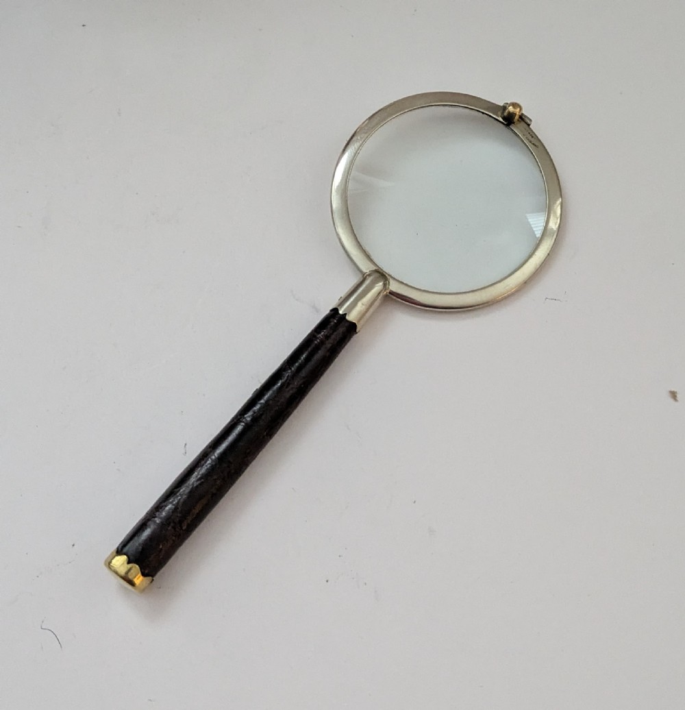 An antique circular magnifying glass with a silver-plated bezel, a dark turned wood handle, and a brass end cap.