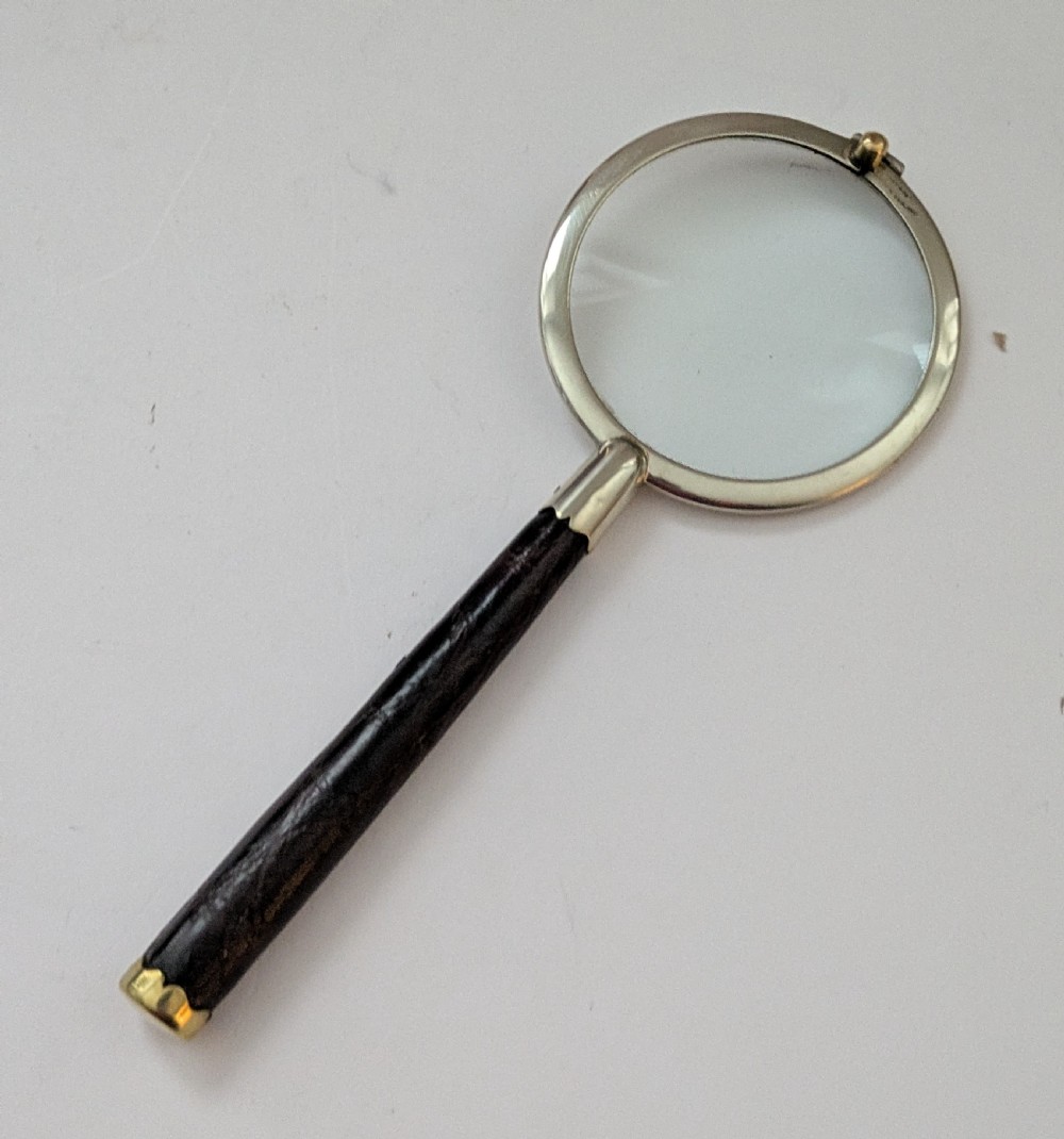 An antique circular magnifying glass with a silver-plated bezel, a dark turned wood handle, and a brass end cap. View III