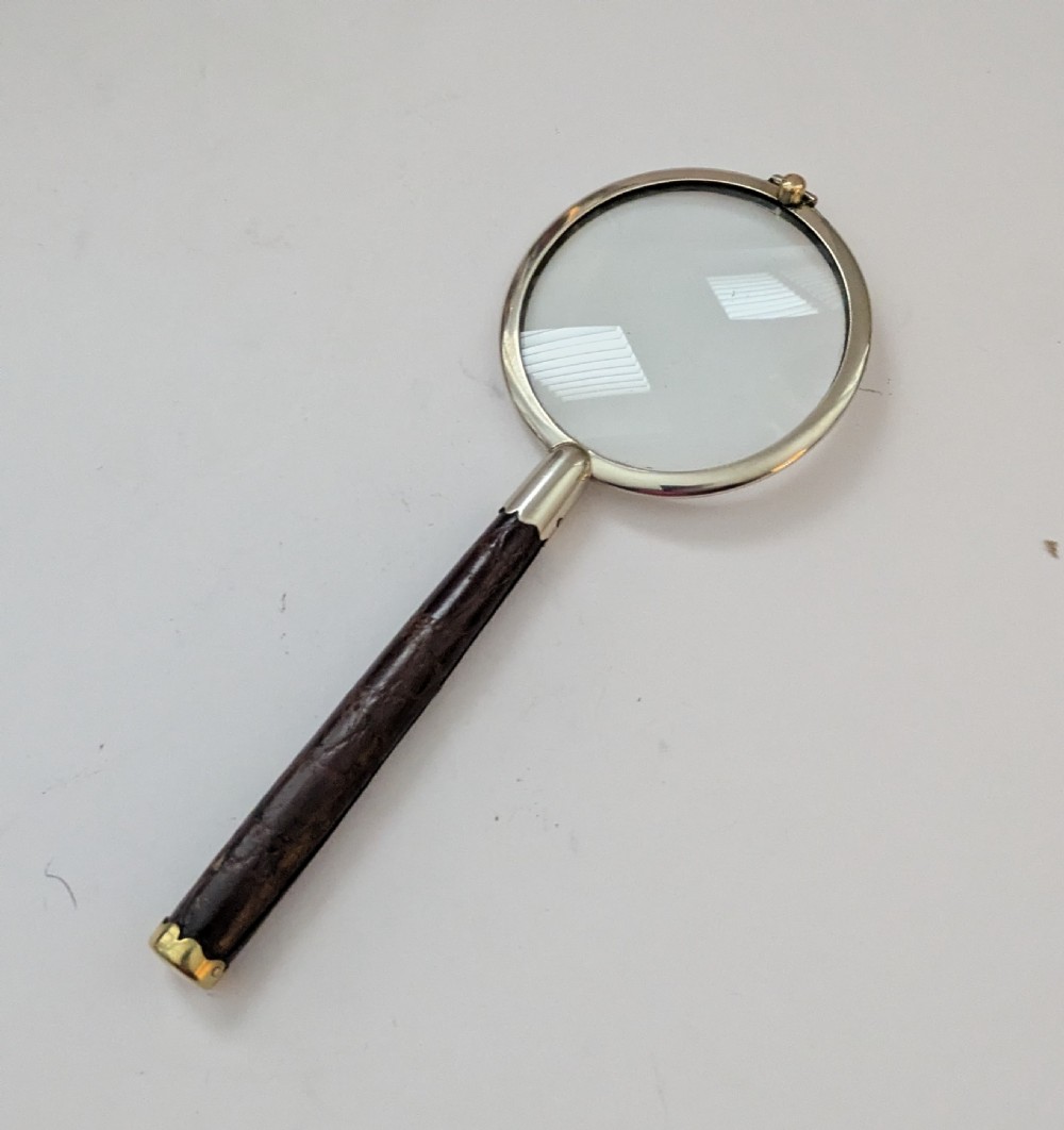 An antique circular magnifying glass with a silver-plated bezel, a dark turned wood handle, and a brass end cap. View V