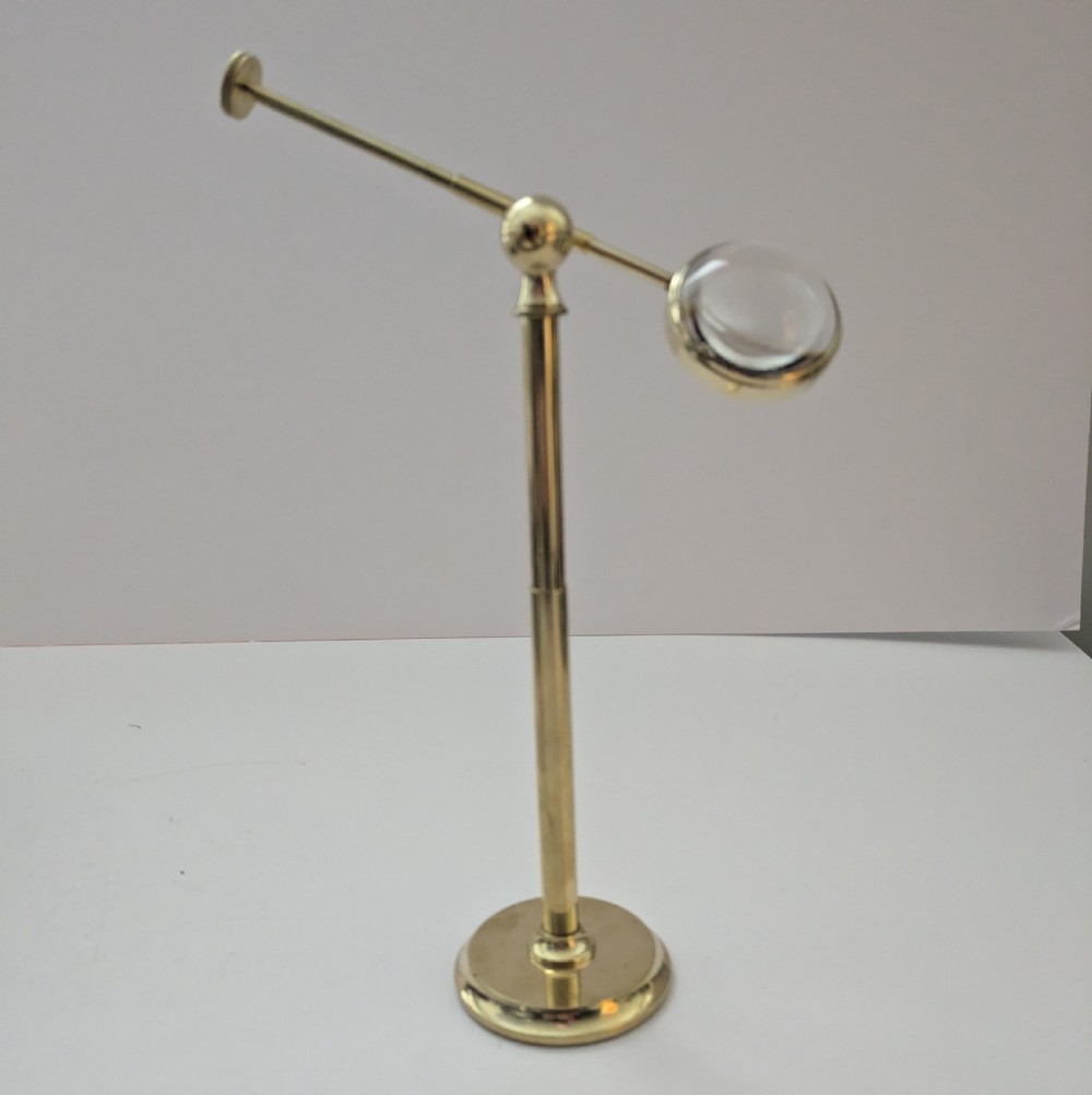 An Edwardian brass standing magnifying glass featuring a circular base, a vertical stem, and an adjustable horizontal arm holding a thick bullseye glass lens. View II