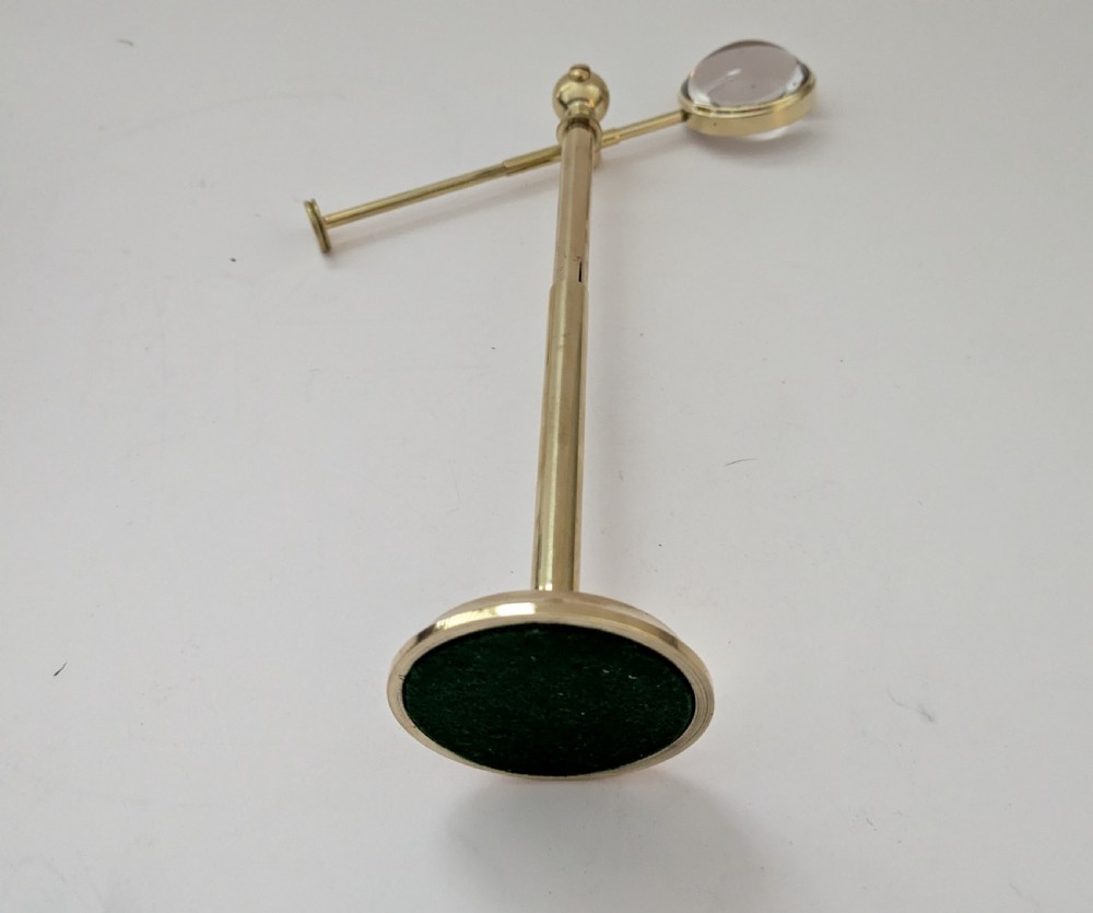 An Edwardian brass standing magnifying glass featuring a circular base, a vertical stem, and an adjustable horizontal arm holding a thick bullseye glass lens. View III