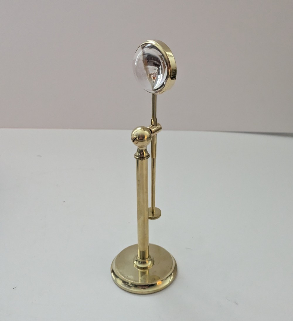 An Edwardian brass standing magnifying glass featuring a circular base, a vertical stem, and an adjustable horizontal arm holding a thick bullseye glass lens. View IV