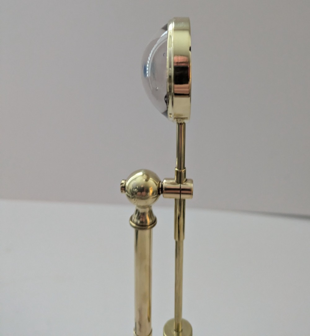 An Edwardian brass standing magnifying glass featuring a circular base, a vertical stem, and an adjustable horizontal arm holding a thick bullseye glass lens. View V