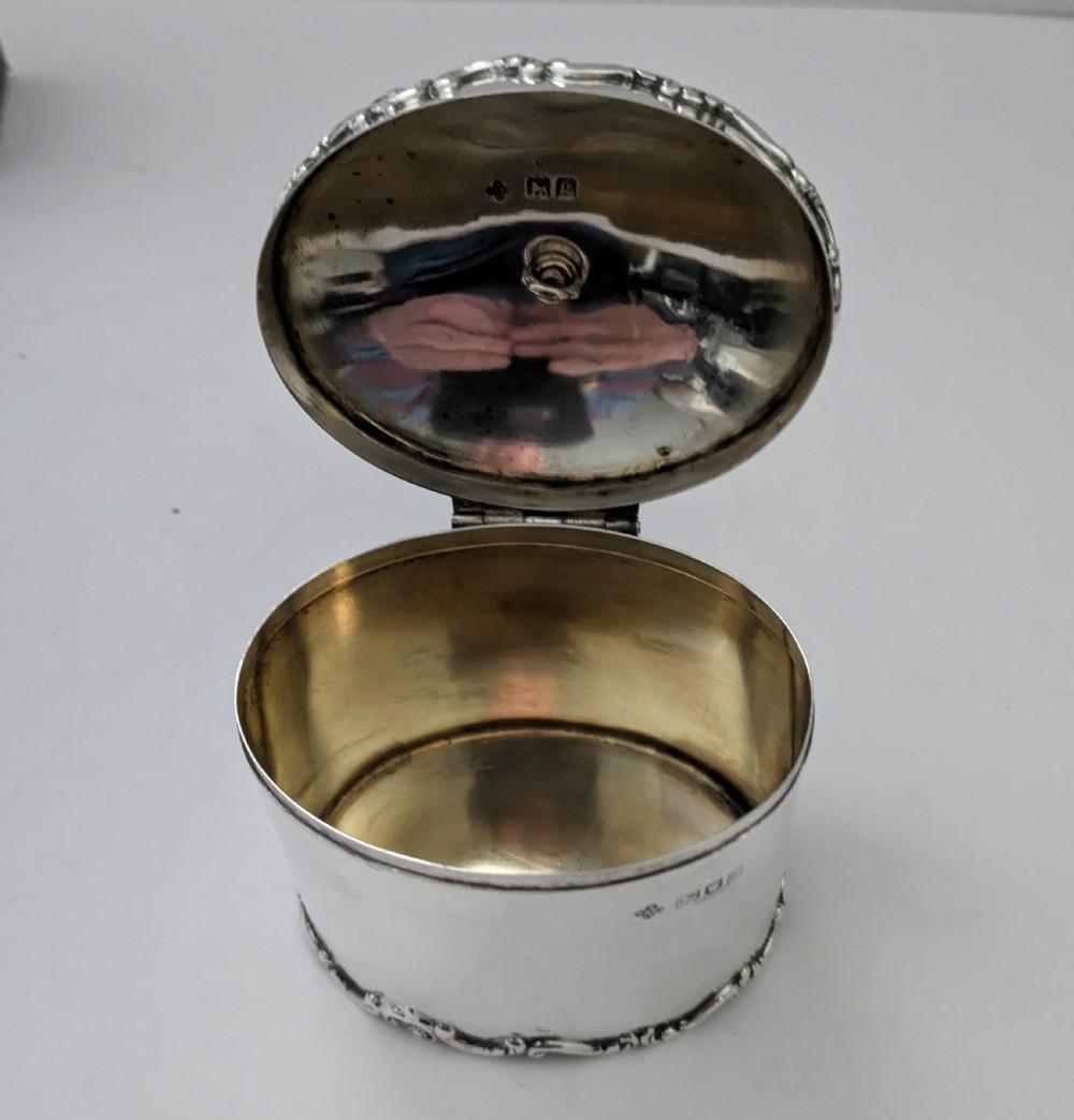 A cylindrical sterling silver tea caddy featuring a scrolled rim border, a fluted finial lid, and stamped London hallmarks on the side. View IV