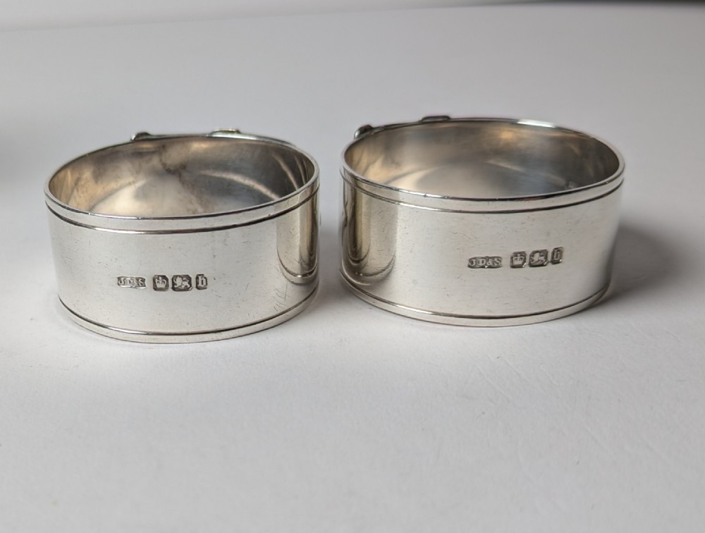 A pair of late Victorian sterling silver napkin rings crafted in the form of buckled belts, shown in front of a black leather presentation case. View VI