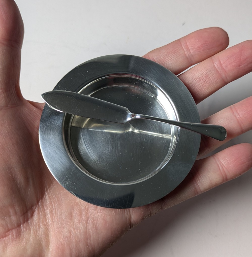 A boxed set of six circular sterling silver butter dishes paired with six matching butter knives inside a silk-lined presentation case. View XVII