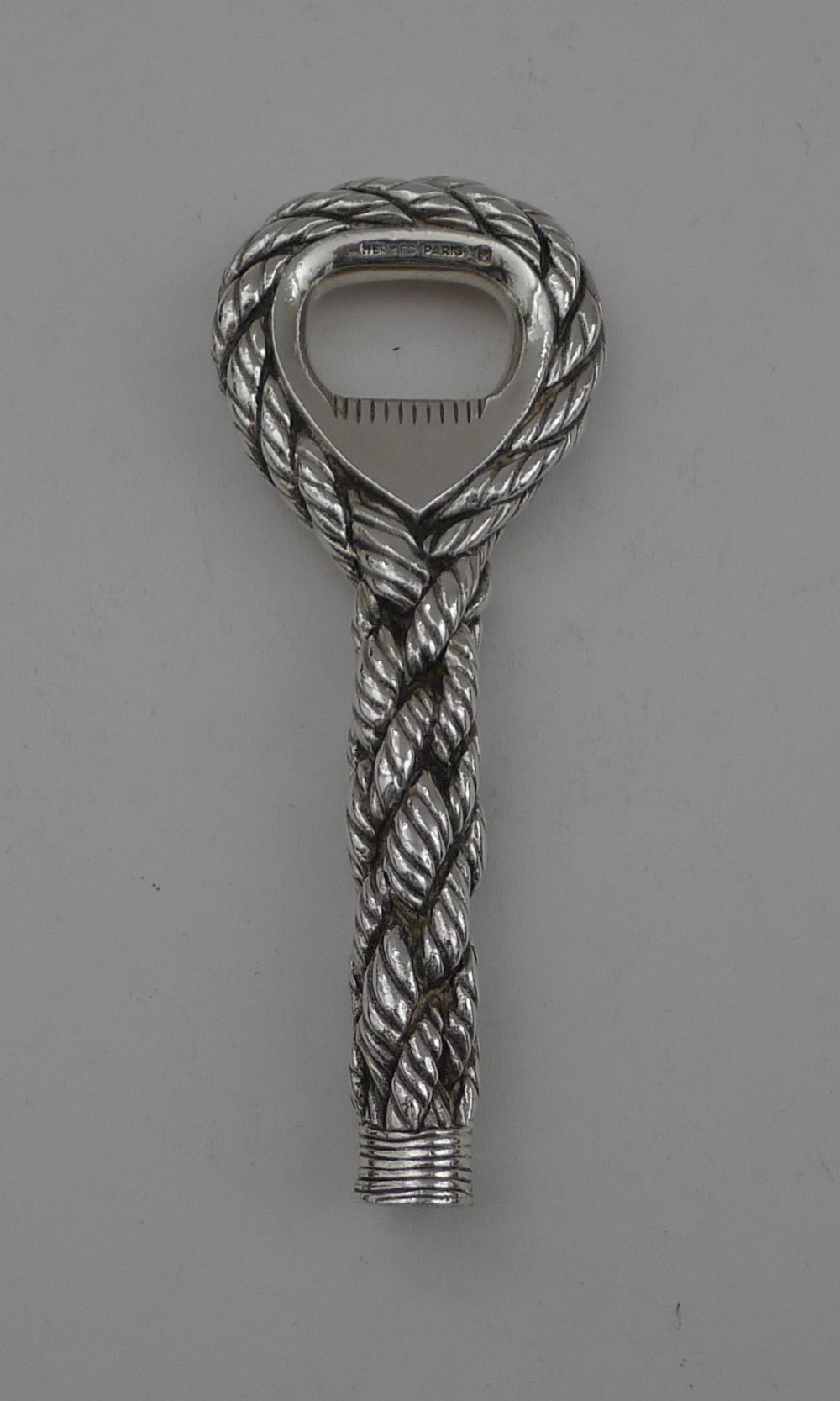 A silver-plated bottle opener featuring a detailed twisted cordage rope handle and a stamped maker mark inside the opener head.