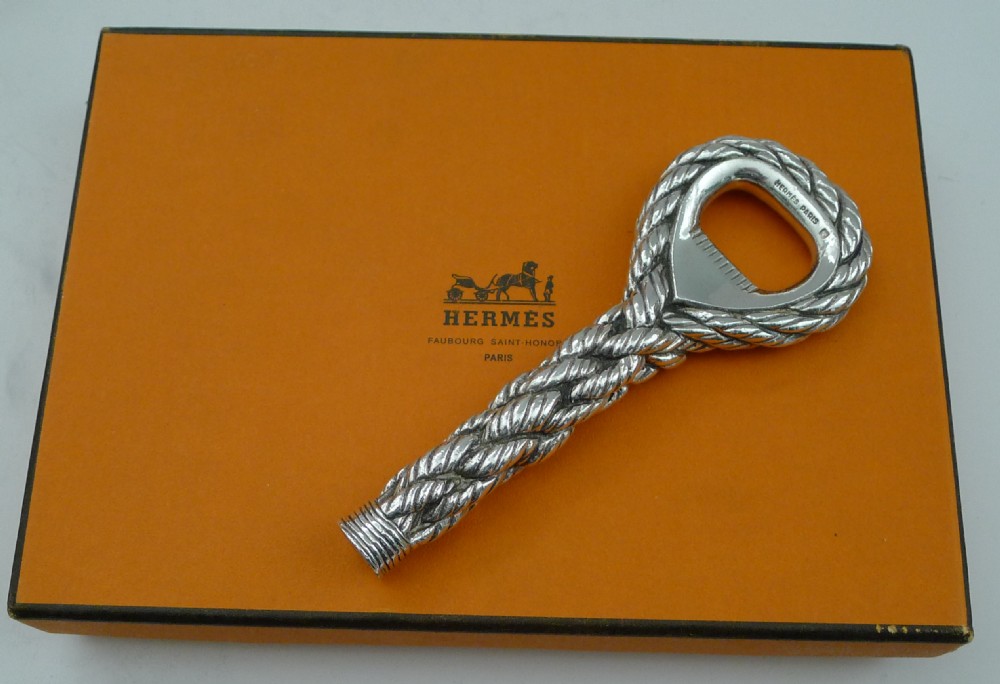 A silver-plated bottle opener featuring a detailed twisted cordage rope handle and a stamped maker mark inside the opener head. View XIII