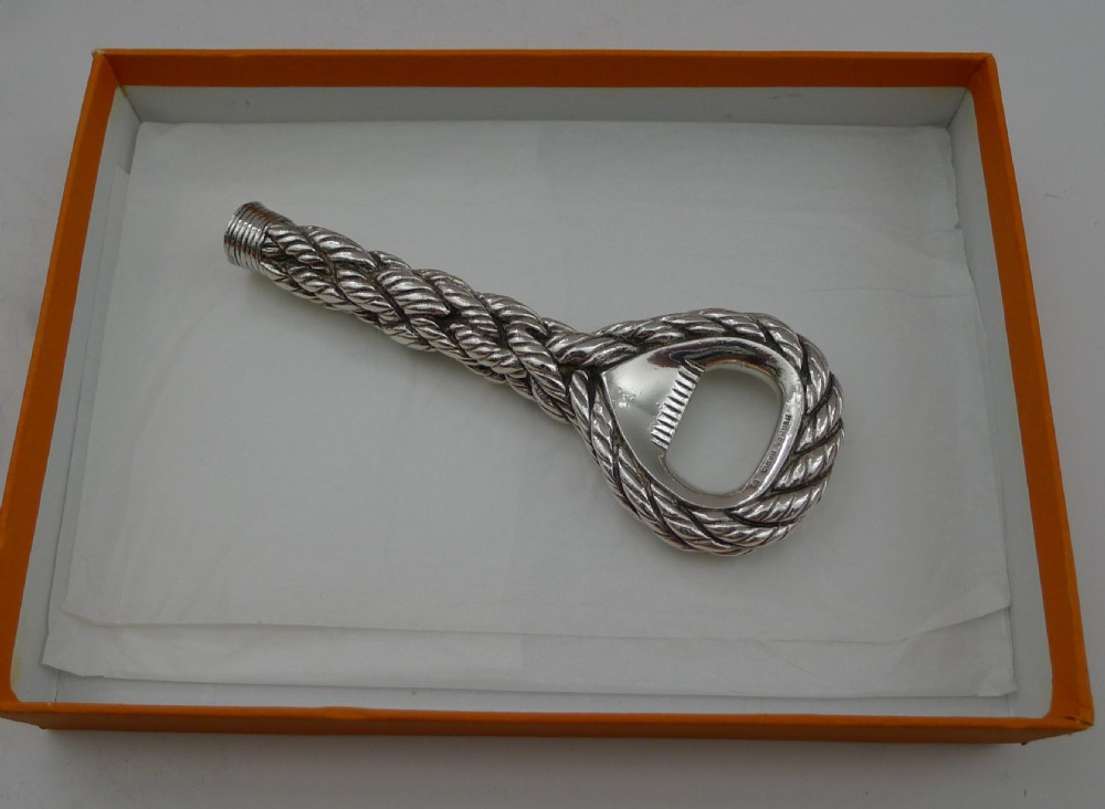 A silver-plated bottle opener featuring a detailed twisted cordage rope handle and a stamped maker mark inside the opener head. View XIV