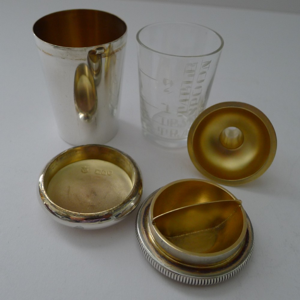 An Edwardian sterling silver travelling medical kit featuring a silver outer sleeve, etched glass dose beaker, and gilded screw caps.