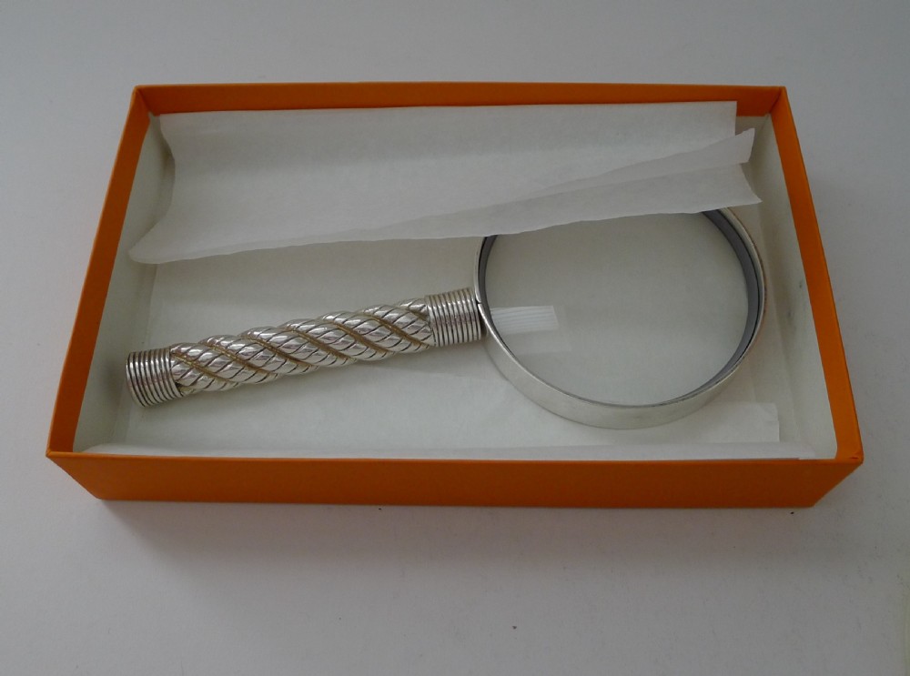 A silver-plated magnifying glass featuring a round frame and a handle styled with a twisted rope motif. View IX