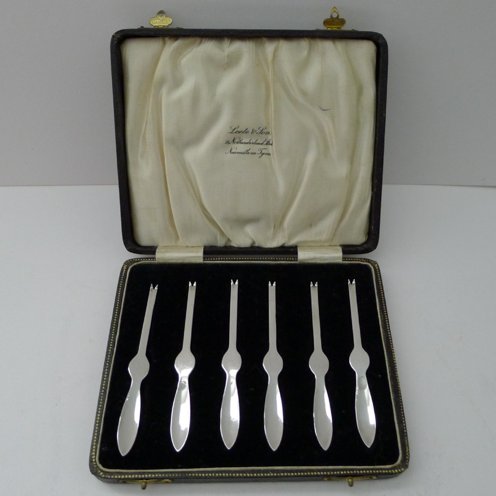 A set of six silver-plated lobster picks arranged in a dark velvet-lined presentation case with a cream silk lid.