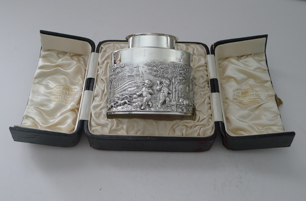 An Edwardian sterling silver tea caddy decorated with repousse embossed cherub scenes and fitted with a smooth cylindrical lid. View XVI