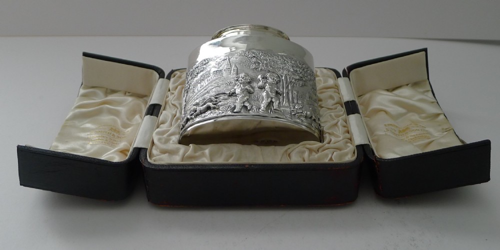 An Edwardian sterling silver tea caddy decorated with repousse embossed cherub scenes and fitted with a smooth cylindrical lid. View XVIII