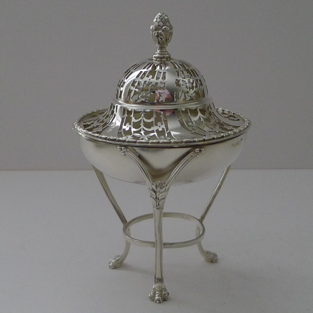 An Edwardian sterling silver pot pourri bowl featuring a pierced domed lid, pineapple finial, and a tripod stand with claw feet.