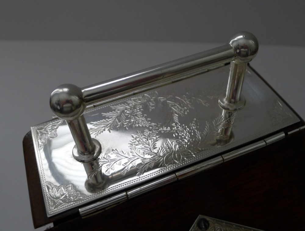A dark oak biscuit box featuring a slanted hinged lid with a silver-plated handle, a blank silver-plated cartouche on the front, and side crest mounts. View IX