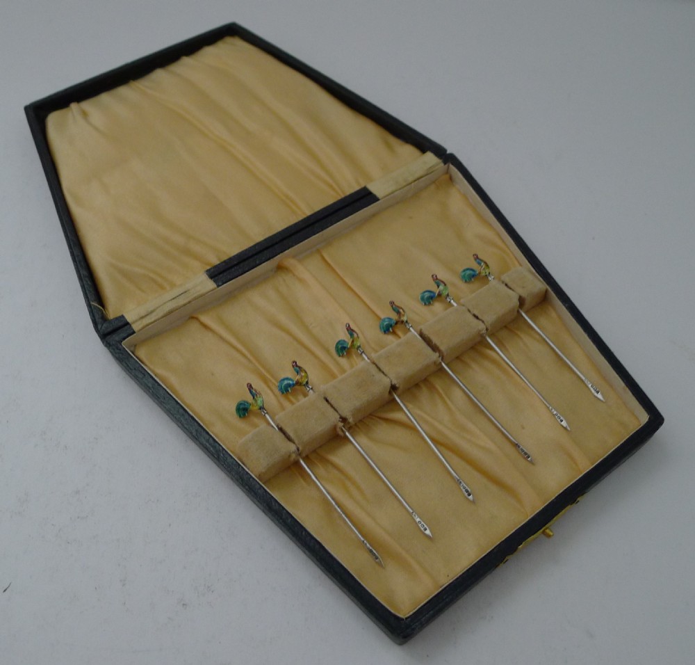 A set of six sterling silver cocktail sticks featuring colourful enamelled cockerel finials inside a silk-lined presentation box. View V