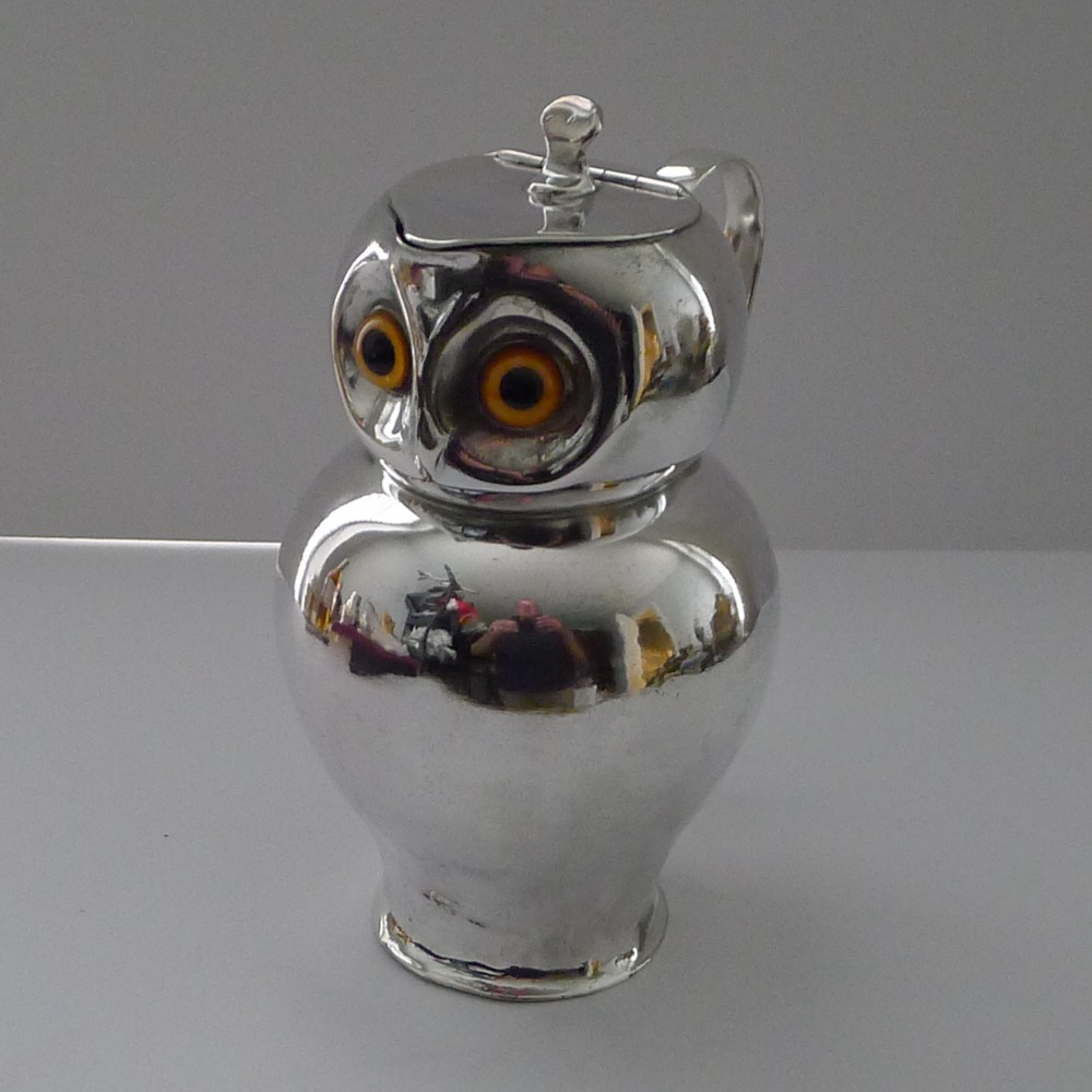 An Edwardian silver-plated jug shaped as an owl with inset yellow and black glass eyes and a hinged lid.
