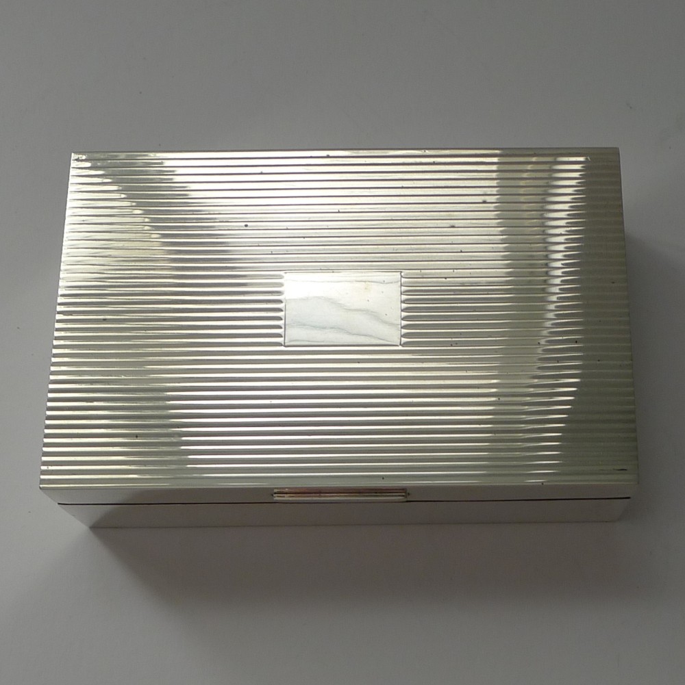 A rectangular sterling silver cigarette box with an engine-turned reeded pattern on the lid and a plain central rectangular cartouche.