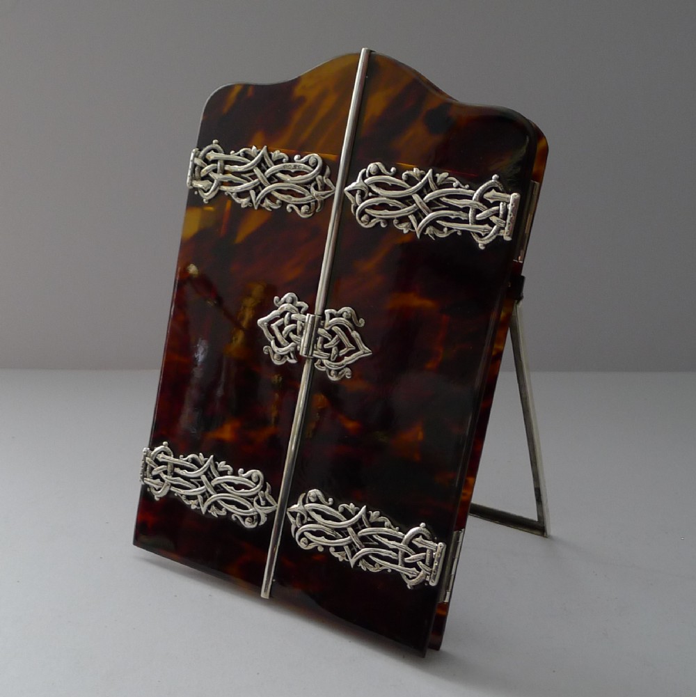 A late 19th-century Victorian tortoiseshell photograph frame featuring arched folding doors, pierced sterling silver mounts, and a silver easel back.