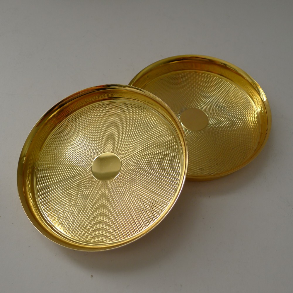 A pair of round gold-coloured vermeil silver gilt coasters featuring engine-turned textured centres and smooth raised rims.