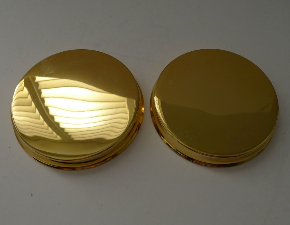 A pair of round gold-coloured vermeil silver gilt coasters featuring engine-turned textured centres and smooth raised rims. View VII