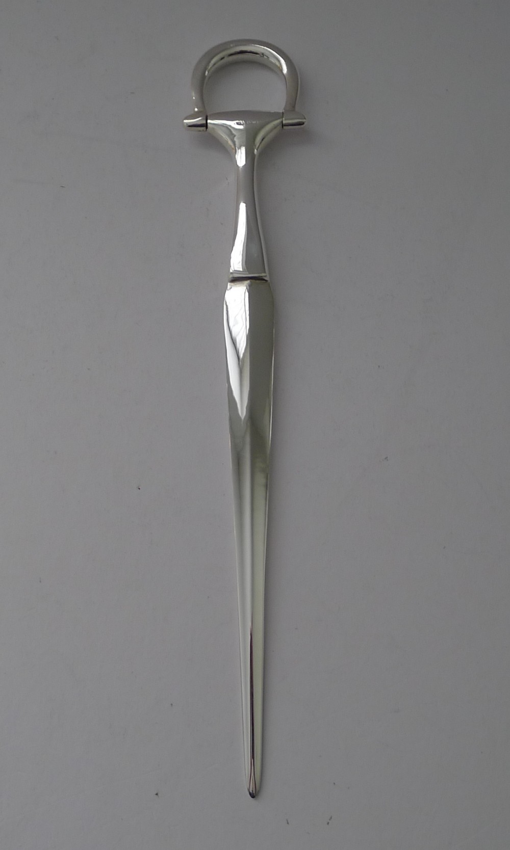 A polished silver letter opener featuring a tapered blade and a handle styled as an equestrian horse bit.