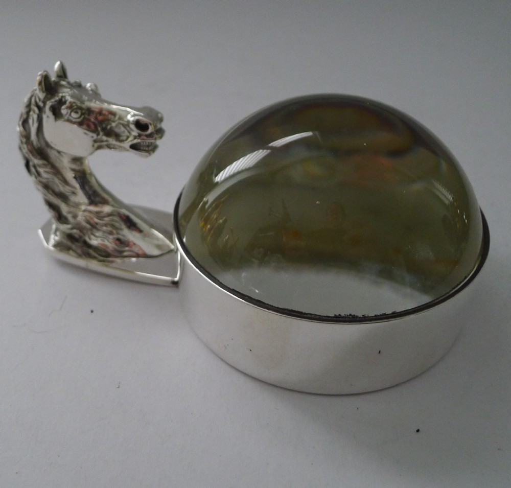 A silver-plated horse head handle joined to a clear glass dome magnifying paperweight.