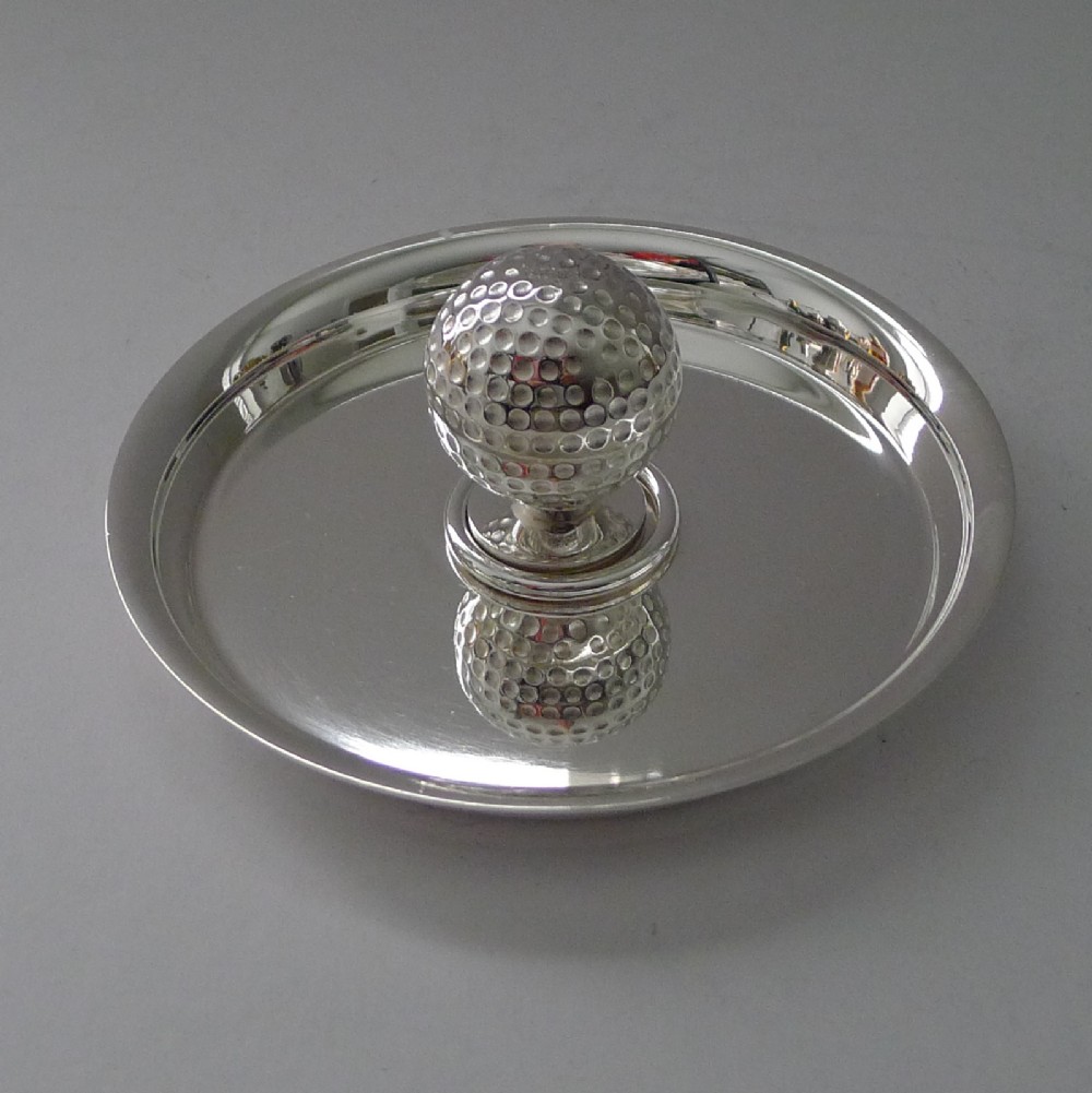 A circular silver-plated shallow dish featuring a central sculpted golf ball handle with a dimpled surface.