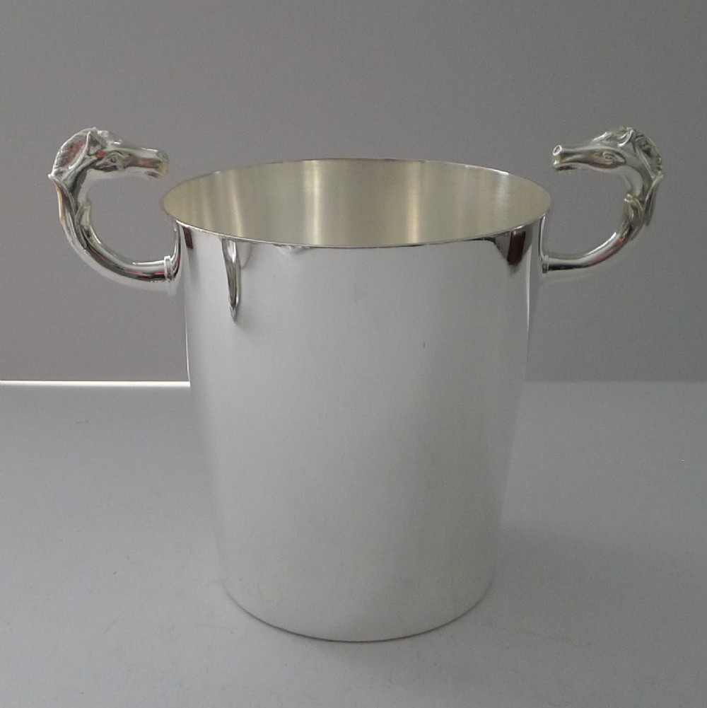 A polished silver-plated ice bucket featuring sculpted horse heads serving as side handles on a smooth cylindrical body.