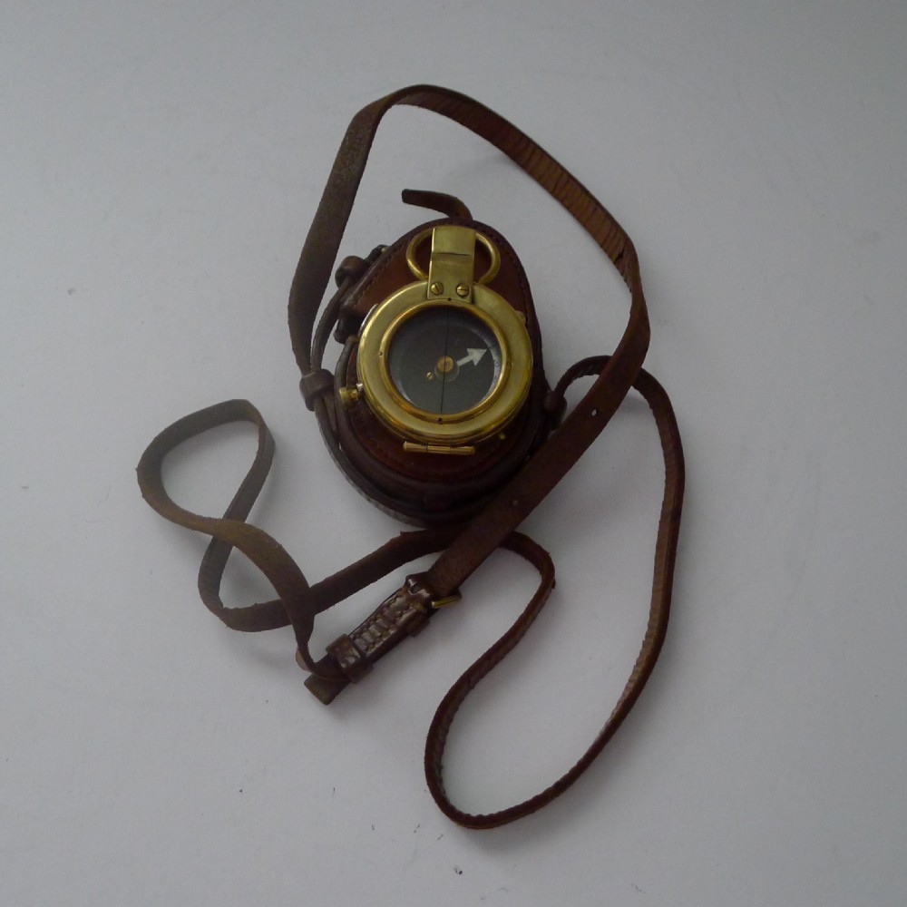 An antique brass Verners pattern military compass housed inside a fitted brown leather carrying case with a long leather strap.