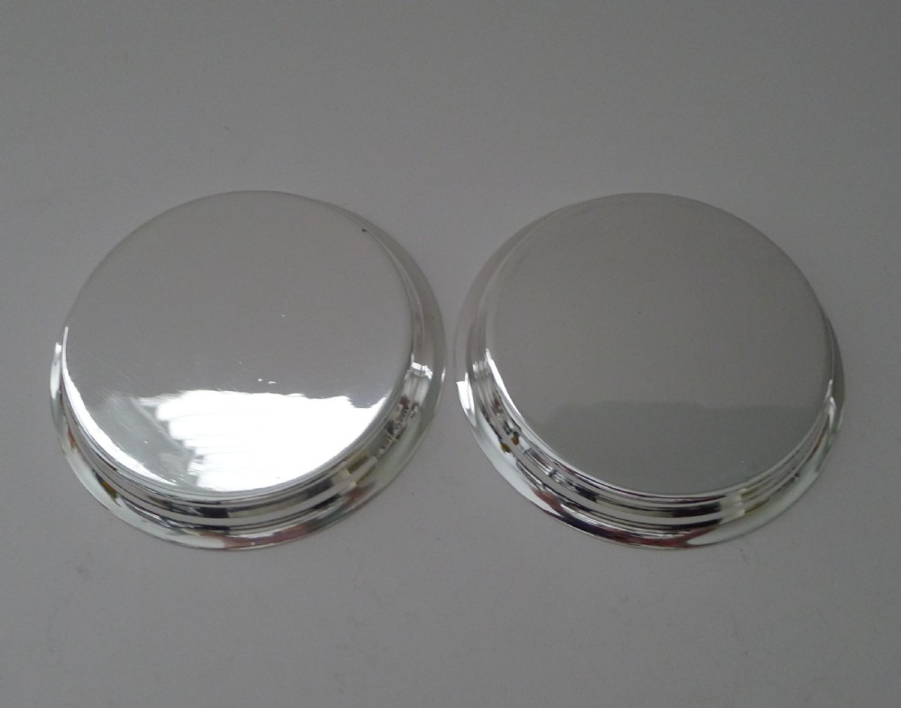 A pair of circular silver-plated coasters featuring raised rims and engine-turned concentric circle patterns. View IV