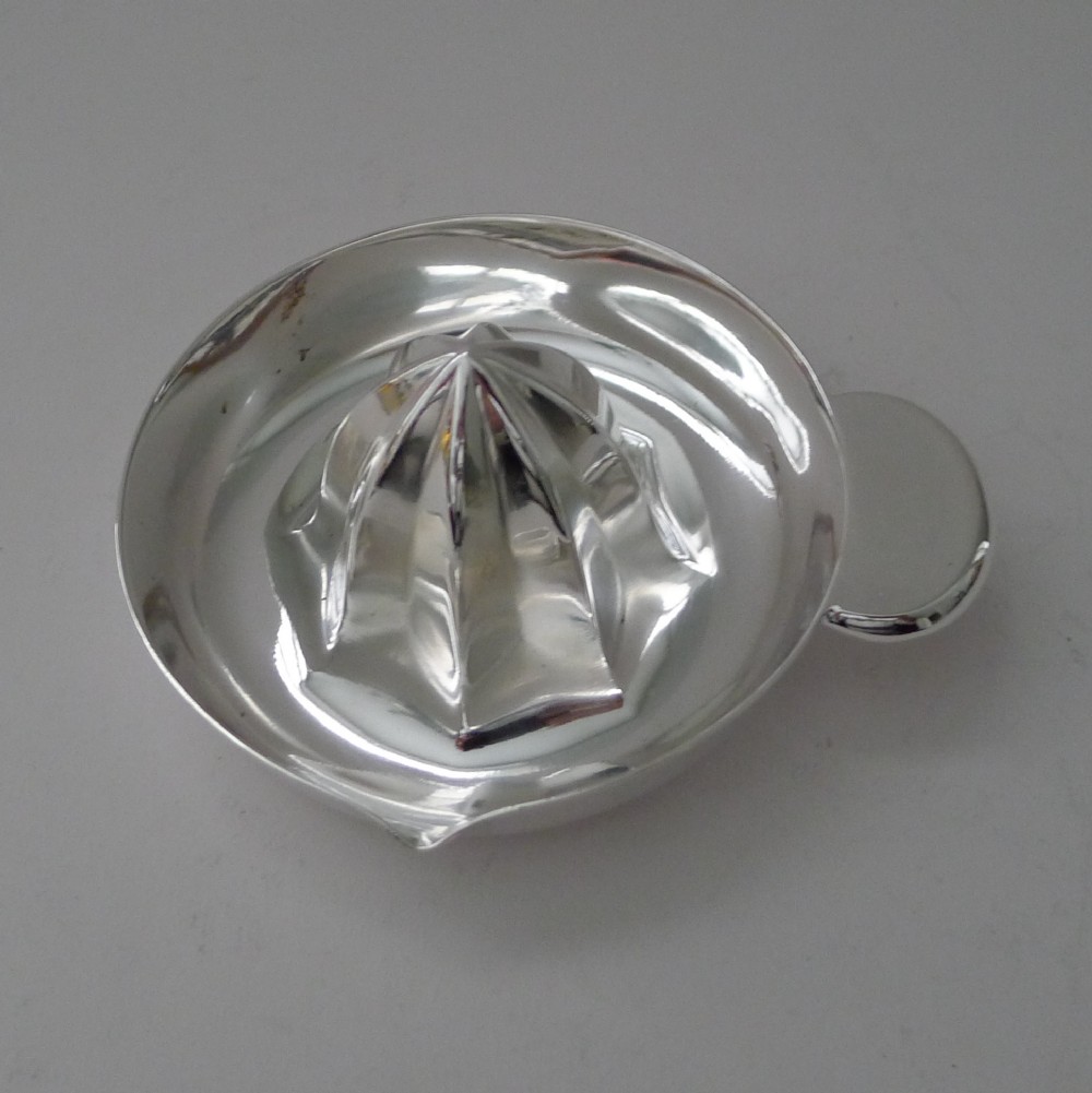 A circular silver-plated Art Deco lemon squeezer featuring a central ridged reaming cone, a side handle, and an integrated spout.