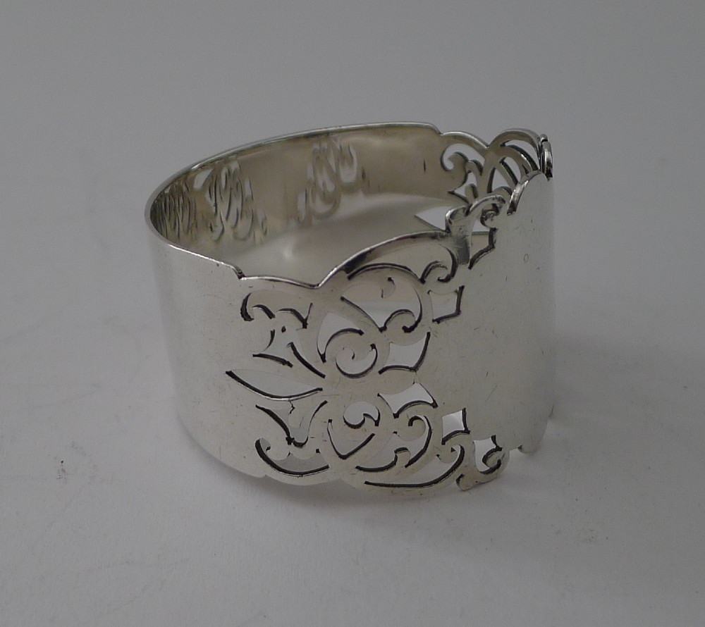 A cylindrical sterling silver napkin ring featuring openwork scroll patterns and an unengraved shield cartouche. View II