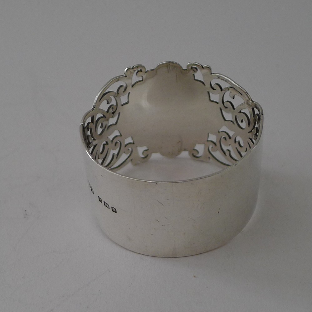 A cylindrical sterling silver napkin ring featuring openwork scroll patterns and an unengraved shield cartouche. View III