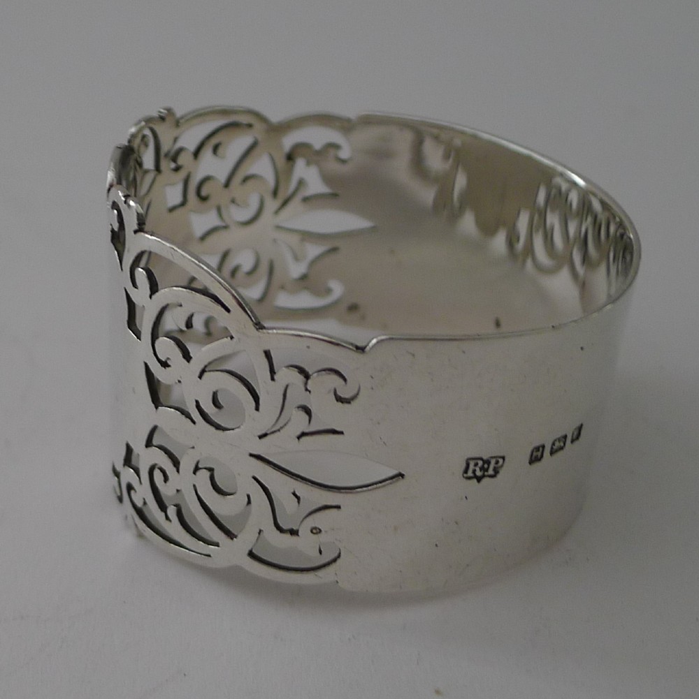 A cylindrical sterling silver napkin ring featuring openwork scroll patterns and an unengraved shield cartouche. View IV