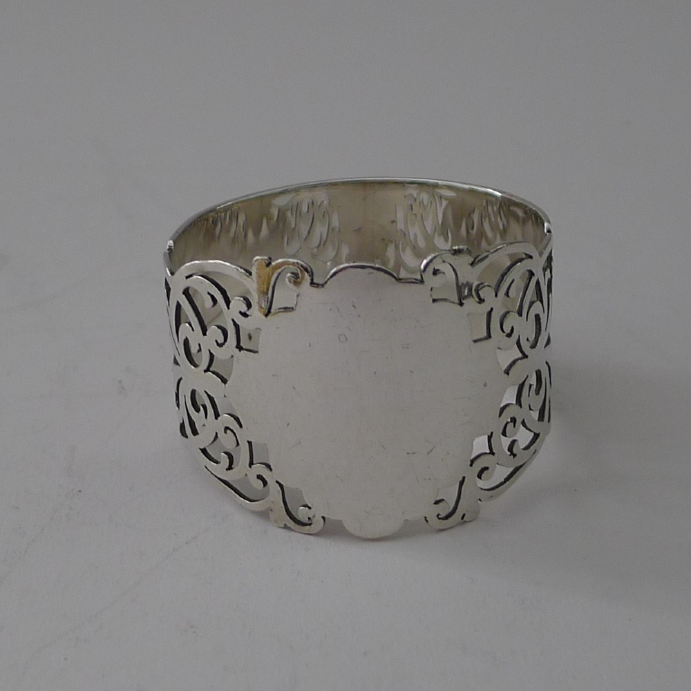A cylindrical sterling silver napkin ring featuring openwork scroll patterns and an unengraved shield cartouche. View VI