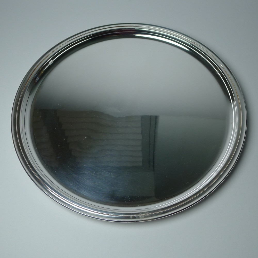 A circular silver-plated drinks tray featuring a flat polished center surface and a stepped moulded rim.