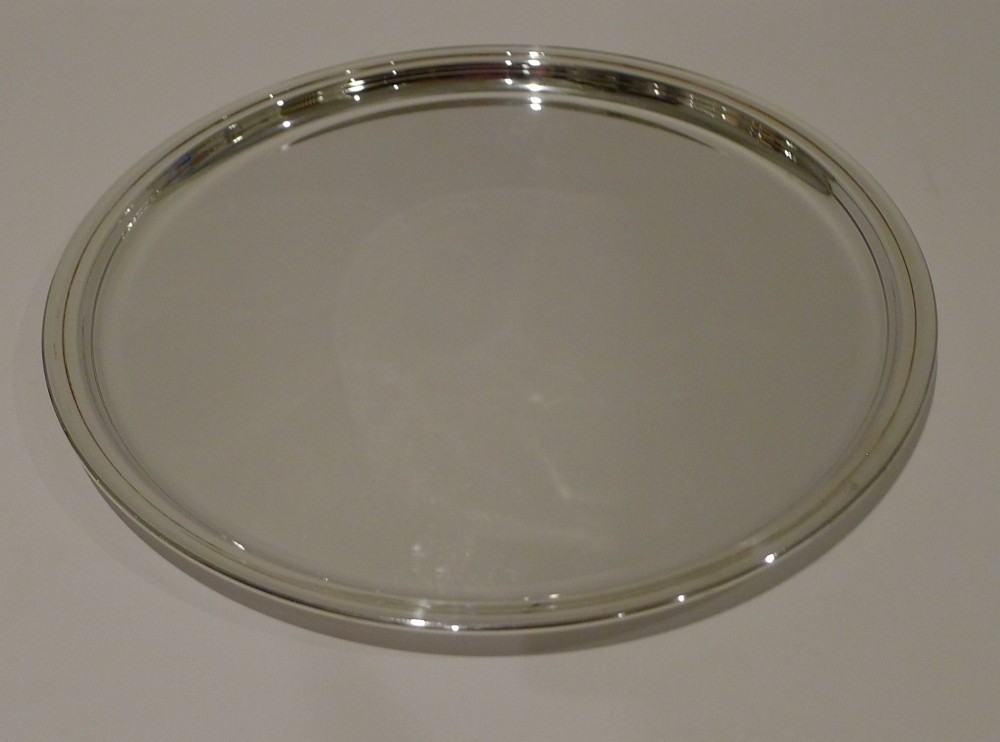 A circular silver-plated drinks tray featuring a flat polished center surface and a stepped moulded rim. View II