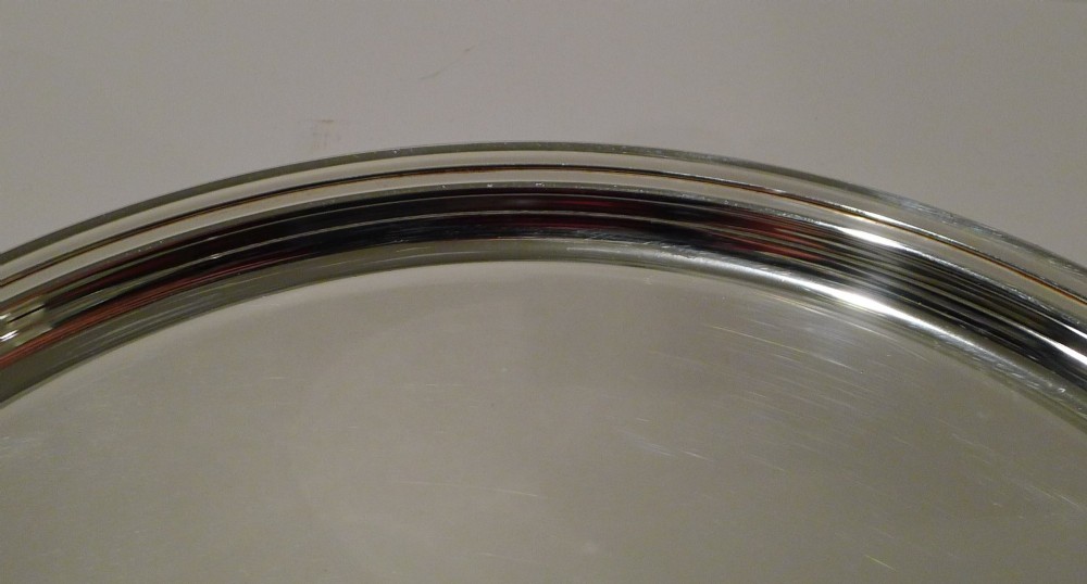 A circular silver-plated drinks tray featuring a flat polished center surface and a stepped moulded rim. View III