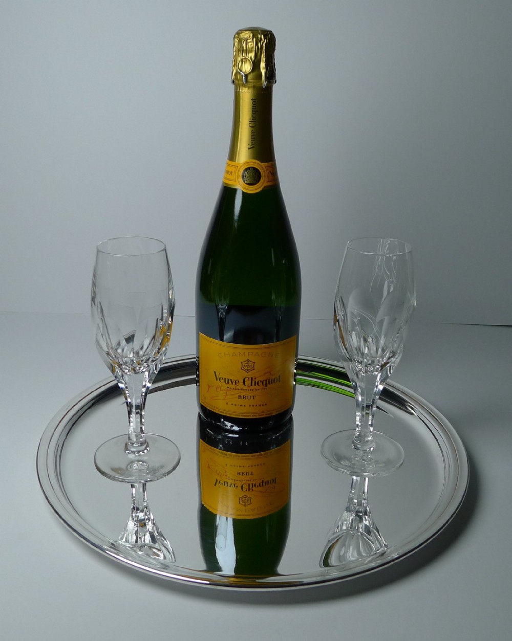 A circular silver-plated drinks tray featuring a flat polished center surface and a stepped moulded rim. View V
