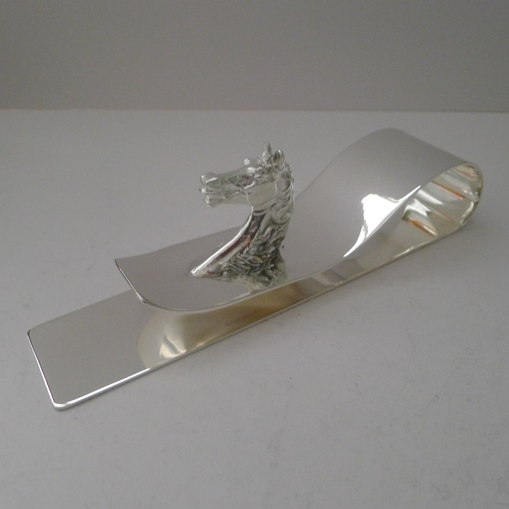 A polished silver-plated bent metal desk clip featuring a detailed sculpted horse head motif. View X