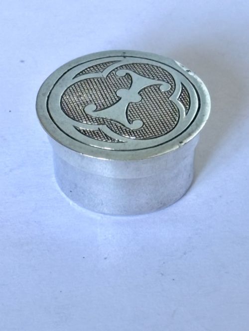 fig 1. A circular sterling silver pyx box featuring an engraved monogram set against a textured hatch pattern on the lid.